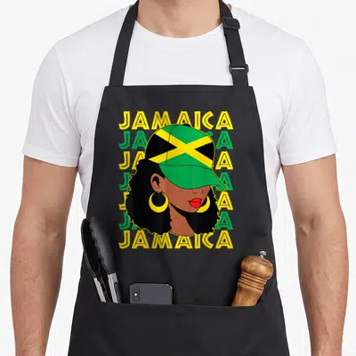 Afro pride apron - Woman with afro and Jamaica flag cap over five stacked Jamaica text lines in green yellow and black — shown on a black cotton canvas apron against a white background
