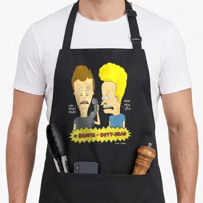 Beavis prank apron - Two cartoon men side-by-side, one holding phone, yellow jagged banner below with red text — shown on a black cotton canvas apron against a white background