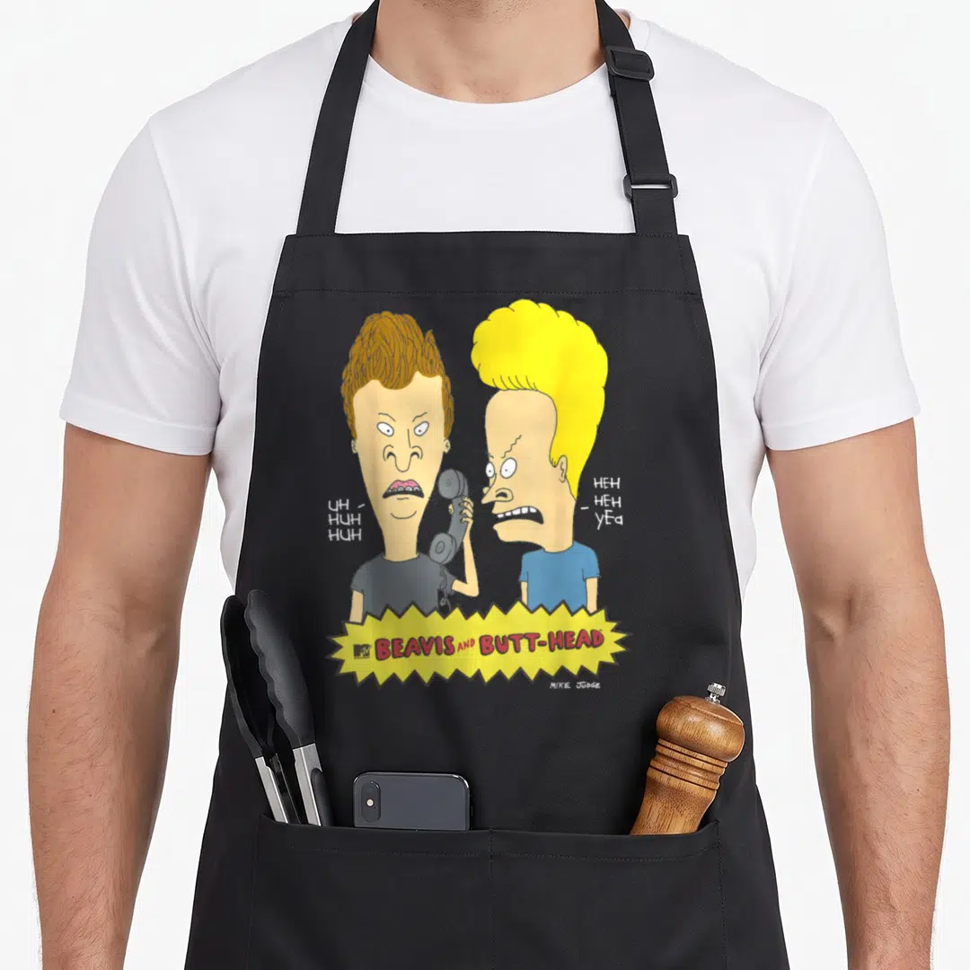 Beavis prank apron - Two cartoon men side-by-side, one holding phone, yellow jagged banner below with red text — shown on a black cotton canvas apron against a white background
