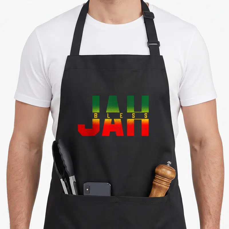 Jah reggae apron - Stacked JAH BLESS JAH text in green yellow red block letters — shown on a black cotton canvas apron against a white background