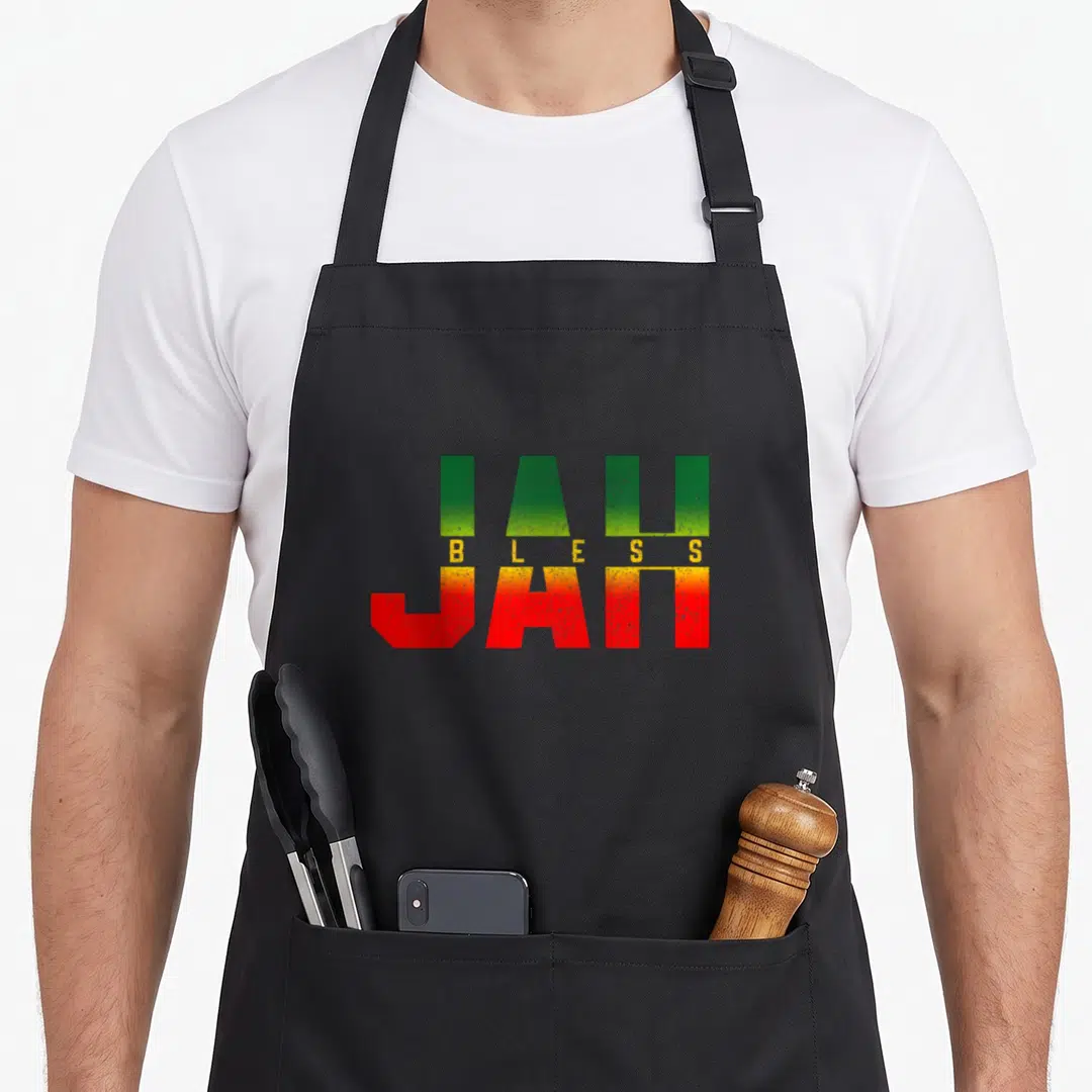 Jah reggae apron - Stacked JAH BLESS JAH text in green yellow red block letters — shown on a black cotton canvas apron against a white background