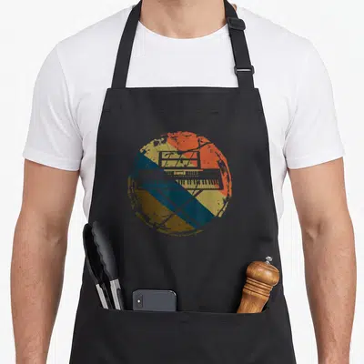 Music musician piano apron - Retro keyboard and laptop silhouette over distressed red orange yellow blue and brown — shown on a black cotton canvas apron against a white background