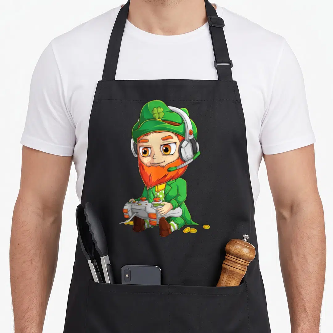 Gamer st patrick day aprons - Cartoon leprechaun with headset holding game controller surrounded by gold coins — shown on a black cotton canvas apron against a white background