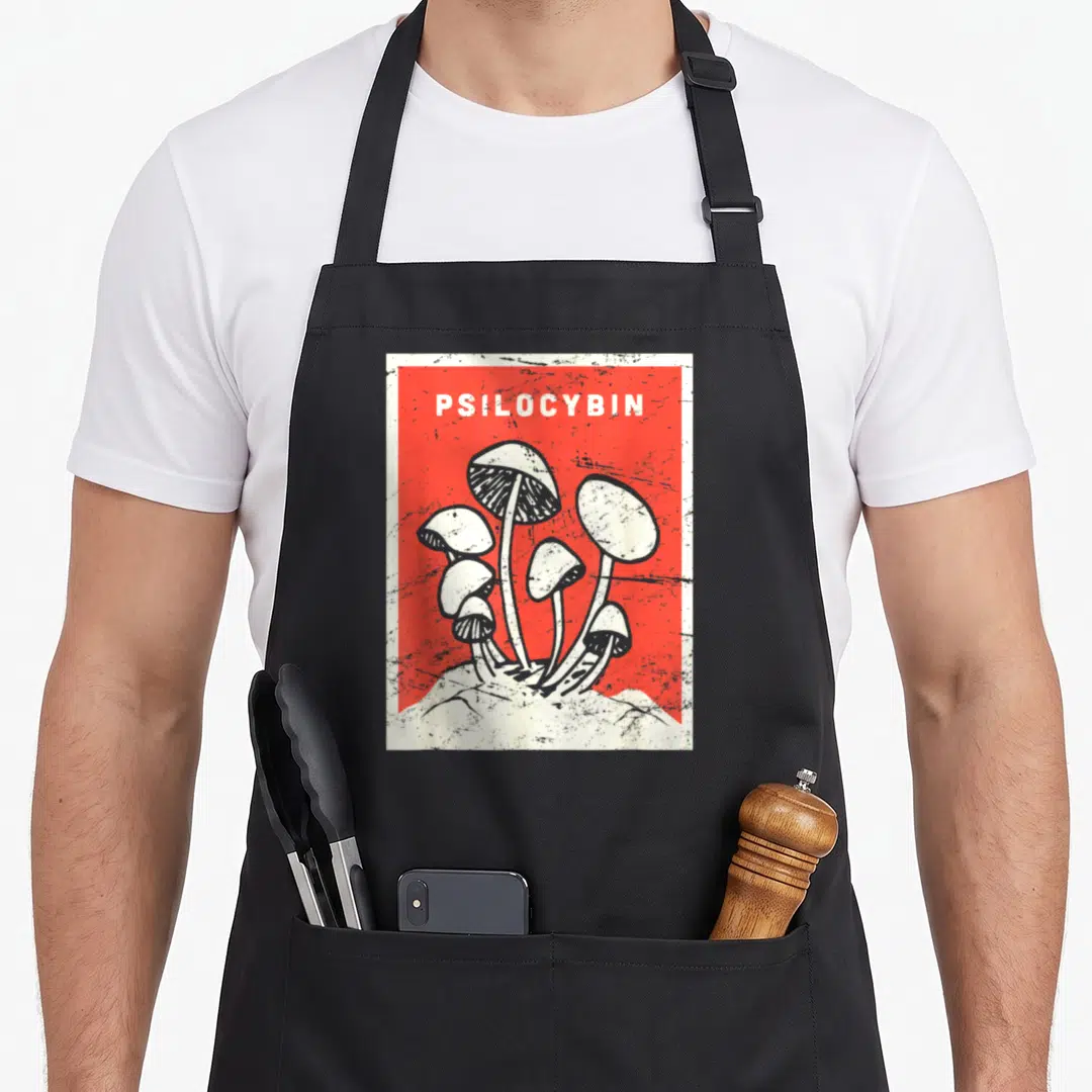 Psilocybin mushroom apron - Distressed red and white graphic of mushroom cluster with PSILOCYBIN text at top — shown on a black cotton canvas apron against a white background
