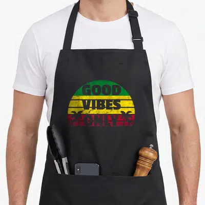 Rasta reggae apron - Distressed semi-circle with GOOD VIBES ONLY text and two palm trees in green yellow red — shown on a black cotton canvas apron against a white background