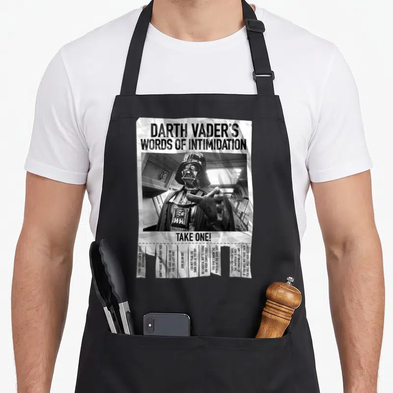 Vader general apron - Darth Vader photo with Words of Intimidation text and vertical quote strips in monochrome — shown on a black cotton canvas apron against a white background