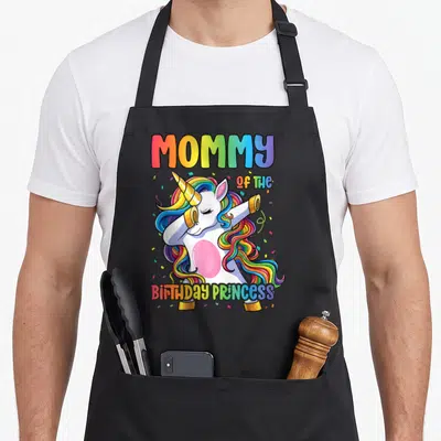 Dabbing princess apron - Rainbow unicorn dabbing with MOMMY OF THE BIRTHDAY PRINCESS text and confetti — shown on a black cotton canvas apron against a white background
