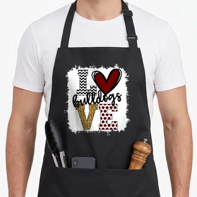 Bulldog mascot apron - I bulldogs VE typography with red heart, chevron, leopard, and polka dot patterns on distressed — shown on a black cotton canvas apron against a white background