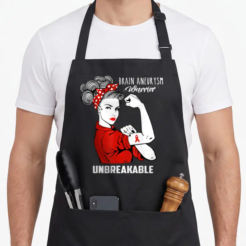 Aneurysm brain apron - Cartoon woman flexing arm with red ribbon and text BRAIN ANEURYSM Warrior UNBREAKABLE — shown on a black cotton canvas apron against a white background