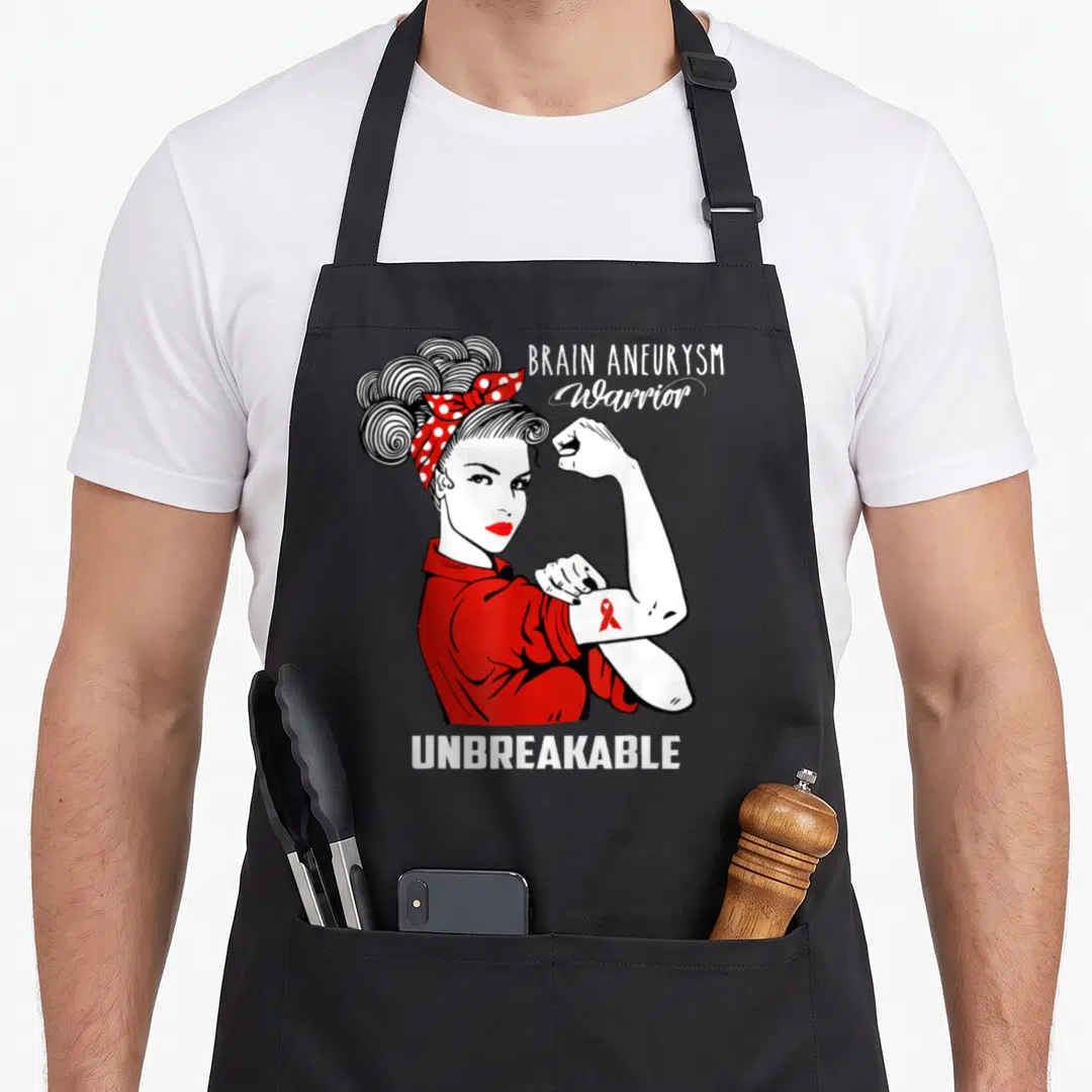 Aneurysm brain apron - Cartoon woman flexing arm with red ribbon and text BRAIN ANEURYSM Warrior UNBREAKABLE — shown on a black cotton canvas apron against a white background