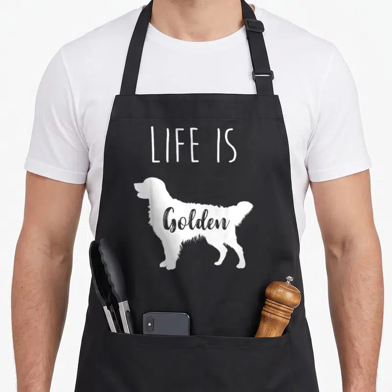 Vintage golden retriever apron - White dog silhouette with LIFE IS above and Golden inside on black background — shown on a black cotton canvas apron against a white background