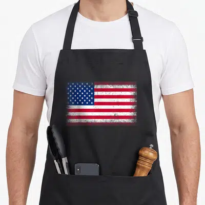 Cute flag 4th of july apron - Distressed red white and blue flag with stars and stripes centered on canvas — shown on a black cotton canvas apron against a white background