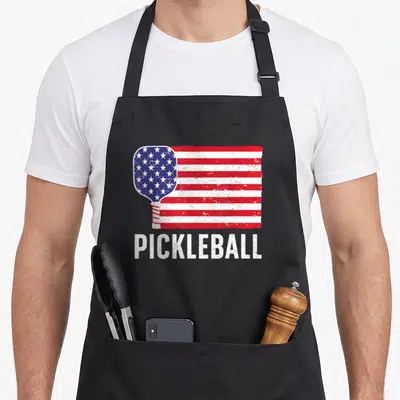 Paddle sport pickleball apron - Distressed paddle filled with US flag pattern and bold white text below — shown on a black cotton canvas apron against a white background