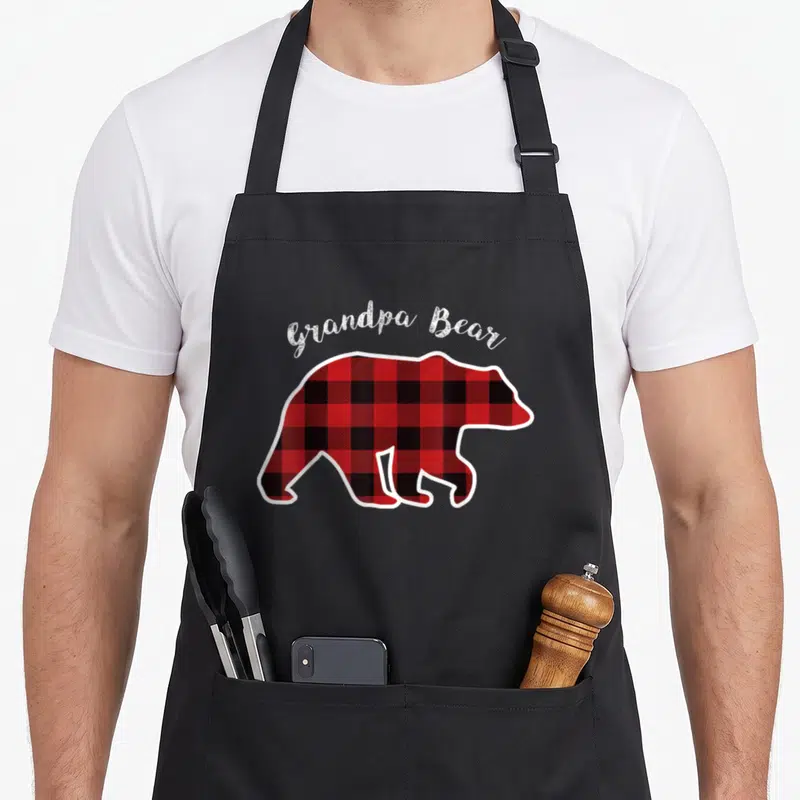 Bear grandpa apron - Red and black plaid bear silhouette with white Grandpa Bear text arched above — shown on a black cotton canvas apron against a white background