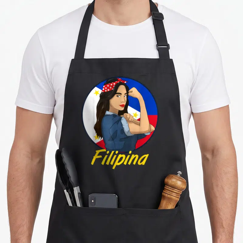 Flag filipino apron - Cartoon woman flexing arm inside circular Philippine flag with yellow Filipina text below — shown on a black cotton canvas apron against a white background