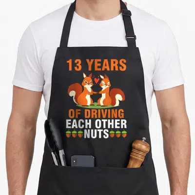 Married each driving aprons - Two orange squirrels holding hands with 13 years text and six acorns flanking the word — shown on a black cotton canvas apron against a white background