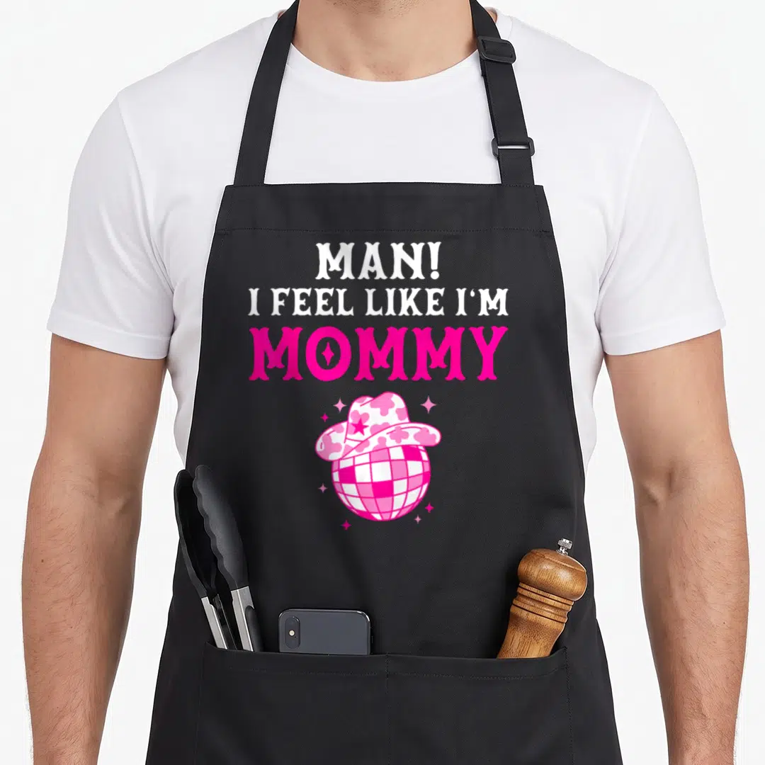 Feel birthday cowgirl aprons - Pink and white disco ball in a cowboy hat below stacked mommy text — shown on a black cotton canvas apron against a white background