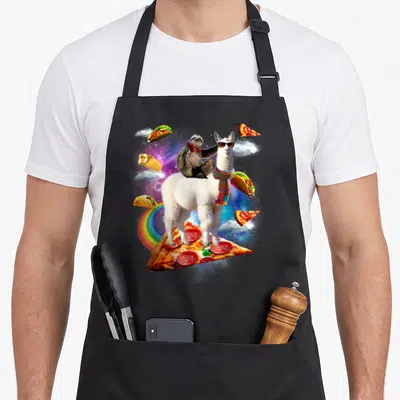 Sloth pizza apron - Llama wearing sunglasses and scarf with sloth on back standing on pizza slice in space with tacos — shown on a black cotton canvas apron against a white background