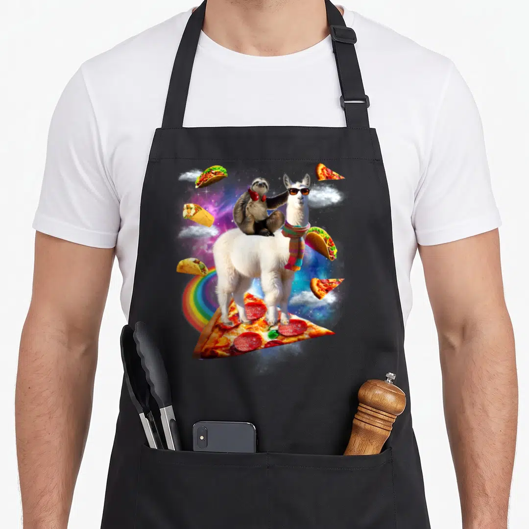 Sloth pizza apron - Llama wearing sunglasses and scarf with sloth on back standing on pizza slice in space with tacos — shown on a black cotton canvas apron against a white background