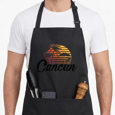 Beach palm mexico apron - Retro striped sunset with palm tree silhouettes and black Cancun script text — shown on a black cotton canvas apron against a white background