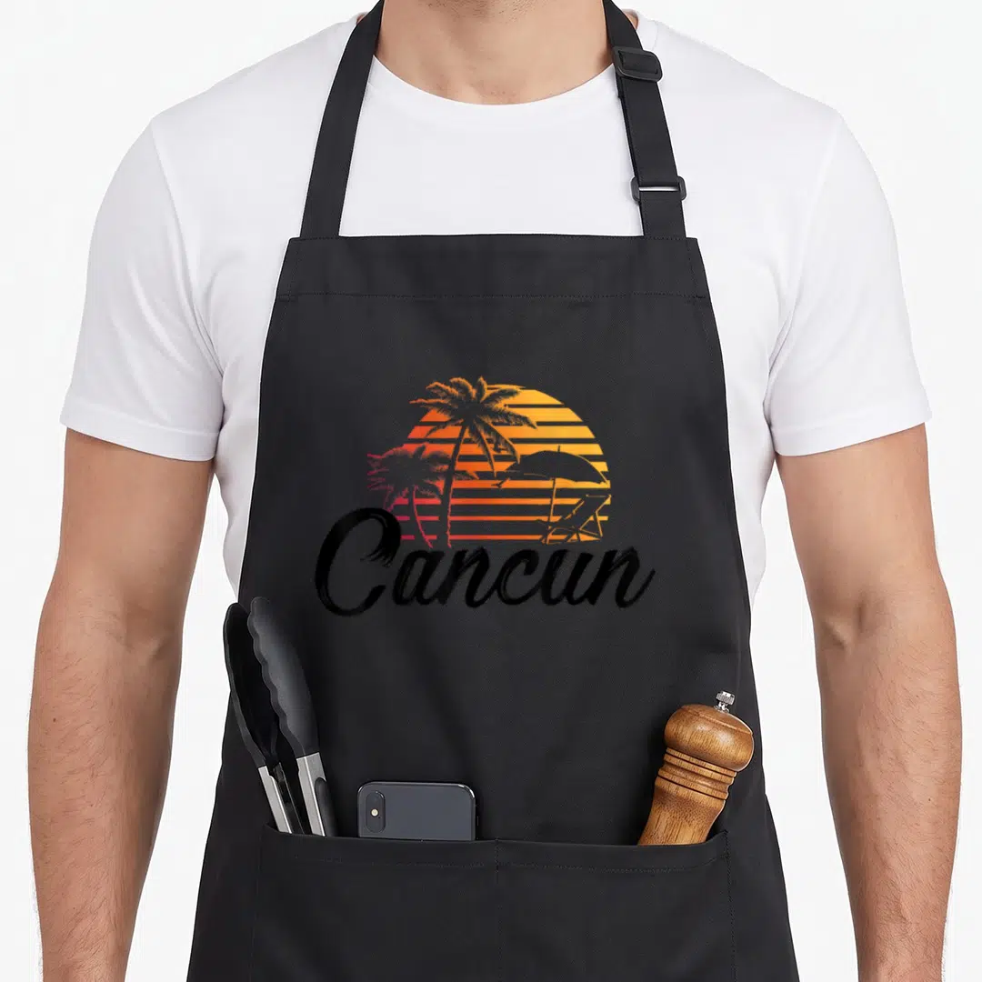 Beach palm mexico apron - Retro striped sunset with palm tree silhouettes and black Cancun script text — shown on a black cotton canvas apron against a white background