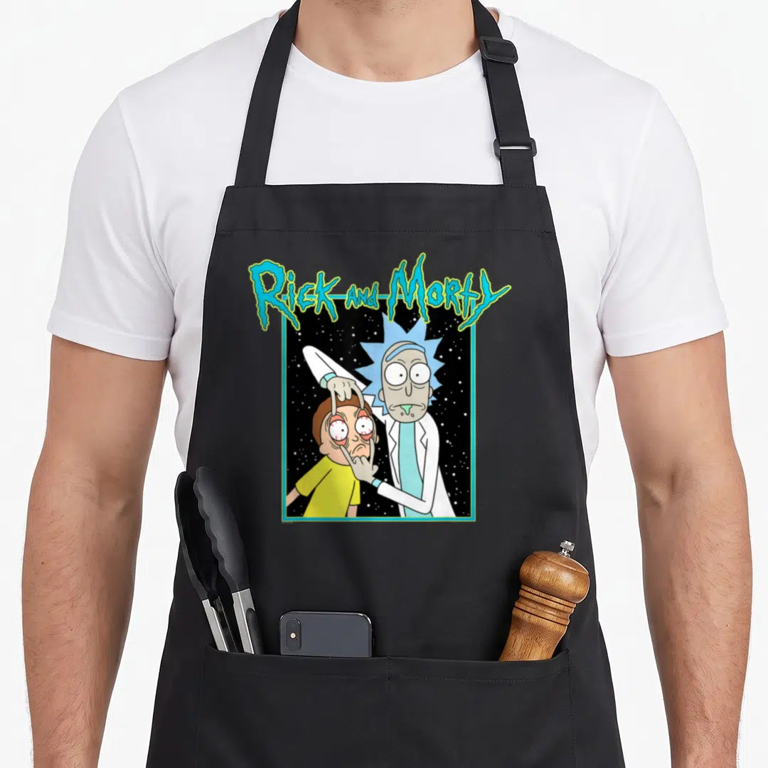 Space cartoon apron - Rick and Morty title text above Rick pulling open Morty's eyes against a starry black background — shown on a black cotton canvas apron against a white background