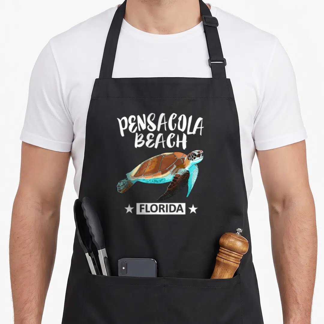 Beach turtle florida apron - Cartoon sea turtle in brown teal white with PENSACOLA BEACH FLORIDA text and two stars — shown on a black cotton canvas apron against a white background