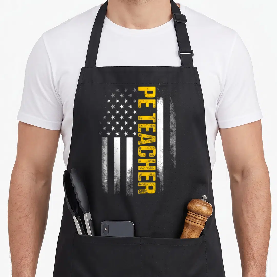 Flag personalized teacher aprons - Vertical yellow PE TEACHER text overlaid on distressed white USA flag stars — shown on a black cotton canvas apron against a white background
