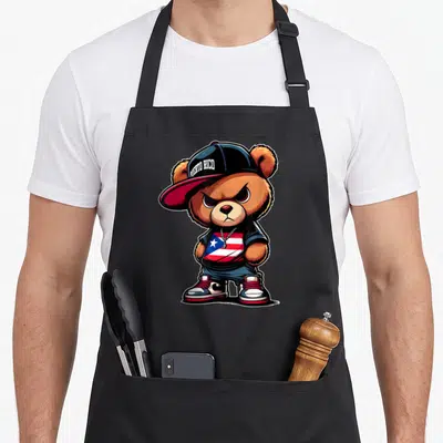 Puerto teddy bear apron - Cartoon brown bear wearing a cap with PUERTO RICO text and a red white and blue flag shirt — shown on a black cotton canvas apron against a white background