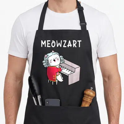 Classical piano apron - Cartoon white cat in red coat playing piano under MEOWZART text — shown on a black cotton canvas apron against a white background