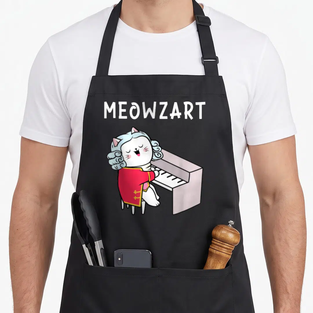 Classical piano apron - Cartoon white cat in red coat playing piano under MEOWZART text — shown on a black cotton canvas apron against a white background