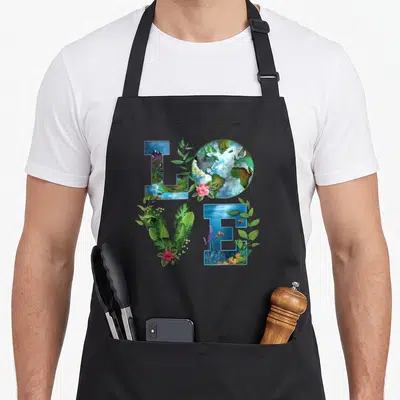 Planet everyday apron - LOVE text with mountains earth leaves and underwater fish in watercolor — shown on a black cotton canvas apron against a white background