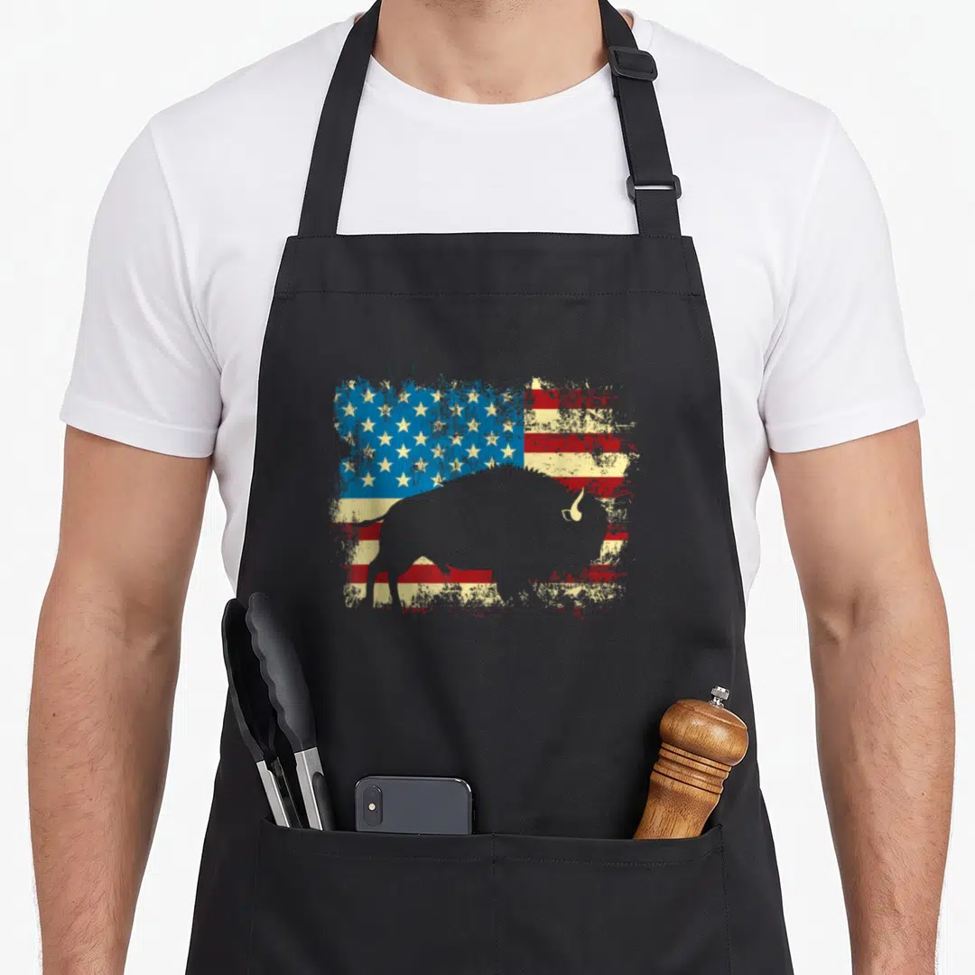 Wildlife american flag apron - Grey bison silhouette over distressed red white blue USA flag pattern — shown on a black cotton canvas apron against a white background