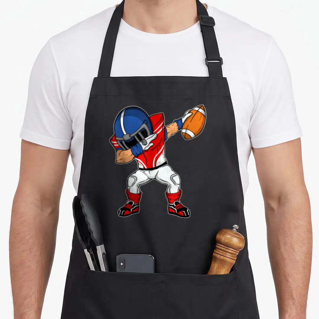 Dabbing football apron - Cartoon football player in red and blue uniform dabbing while holding an orange ball — shown on a black cotton canvas apron against a white background