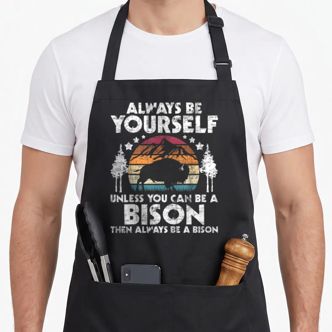 Alway buffalo apron - Bison silhouette in front of striped sun and mountains with white text and stars — shown on a black cotton canvas apron against a white background