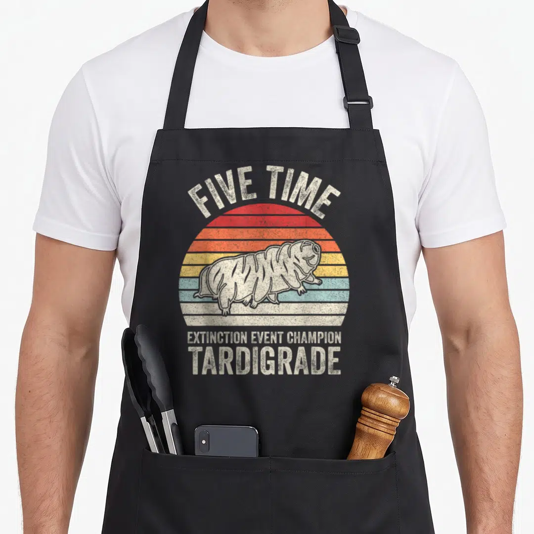 Microbiology biologist apron - Tardigrade illustration over striped sun with text FIVE TIME EXTINCTION EVENT CHAMPION — shown on a black cotton canvas apron against a white background