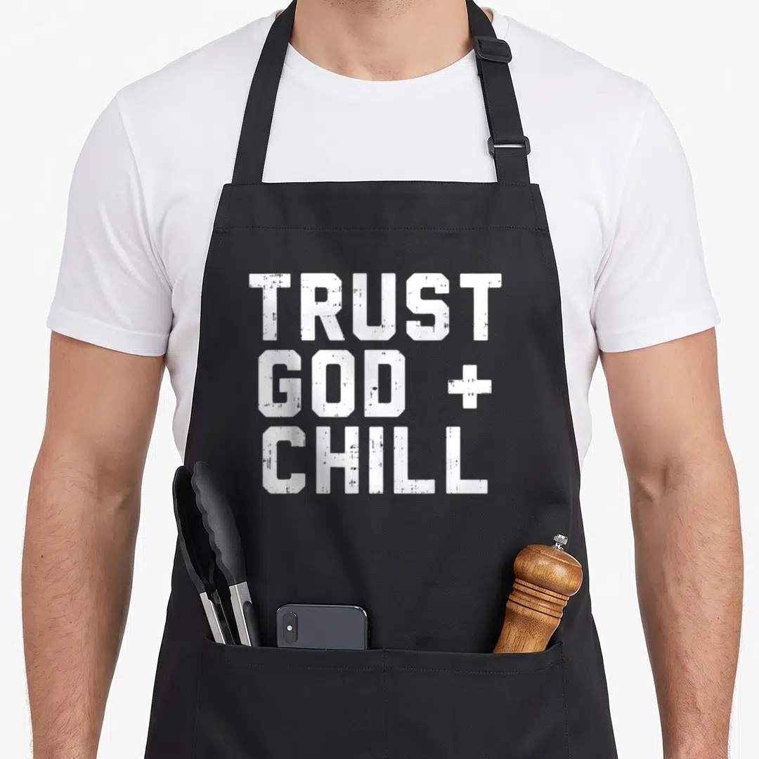 Chill christian apron - White stacked text reading TRUST GOD + CHILL on grey background — shown on a black cotton canvas apron against a white background