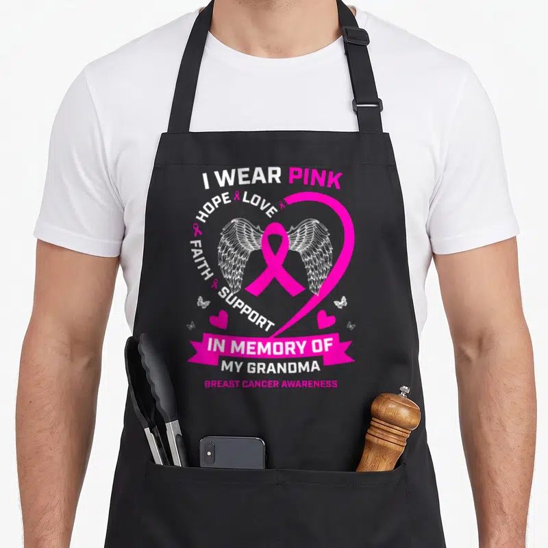 Grandma breast cancer awareness aprons - Pink ribbon with white wings inside a heart surrounded by text I Wear Pink — shown on a black cotton canvas apron against a white background
