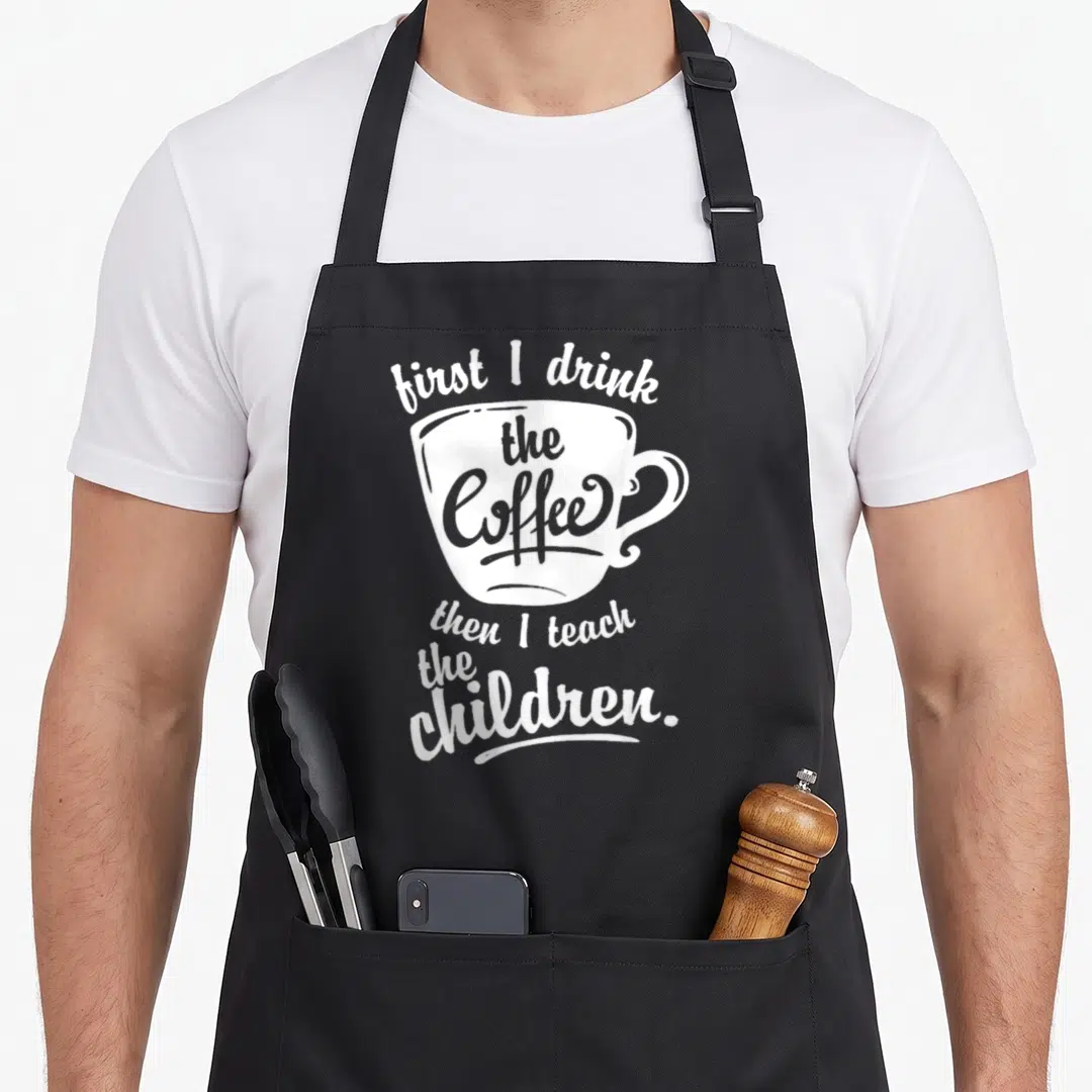 Drink art teacher apron - White coffee cup outline with text first I drink the Coffee then I teach the children — shown on a black cotton canvas apron against a white background