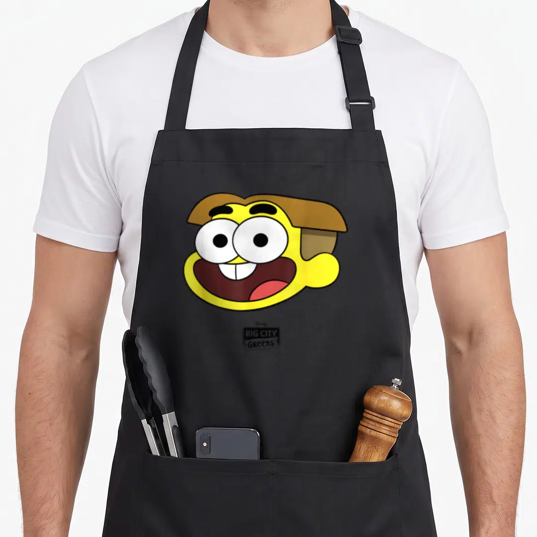 Funny channel cricket apron - Yellow cartoon character head with brown hair and BIG CITY Greens logo below — shown on a black cotton canvas apron against a white background