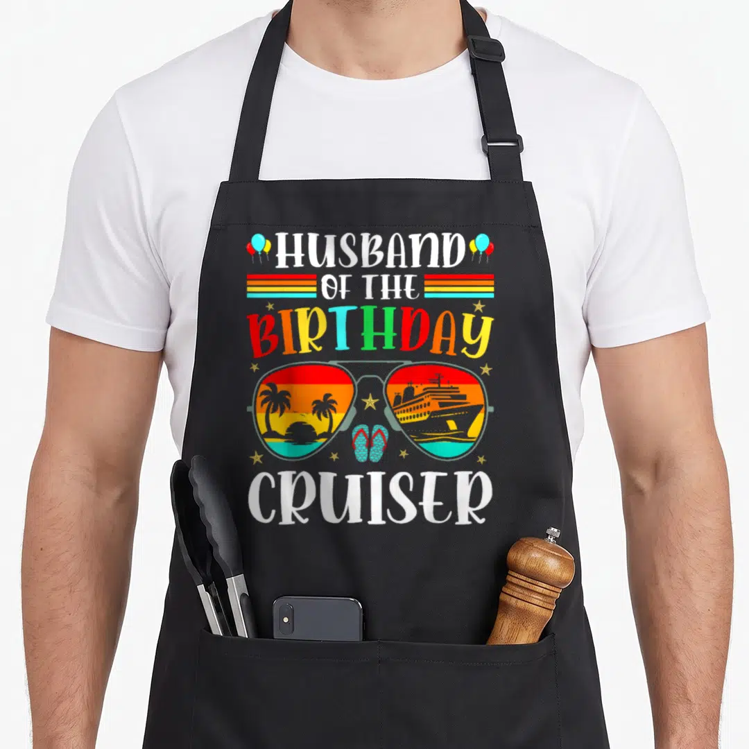 Cruiser husband apron - Sunglasses with beach and ship lenses, text Husband of the Birthday Cruiser — shown on a black cotton canvas apron against a white background