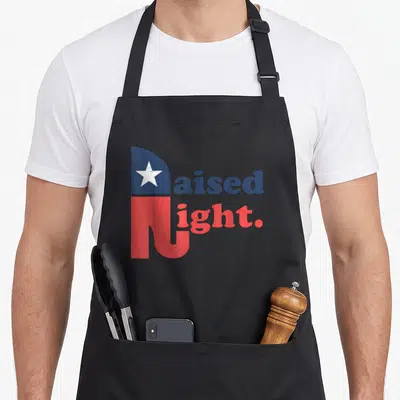 Raised elephant print apron - Raised Right text design with white star in blue and red distressed lettering — shown on a black cotton canvas apron against a white background
