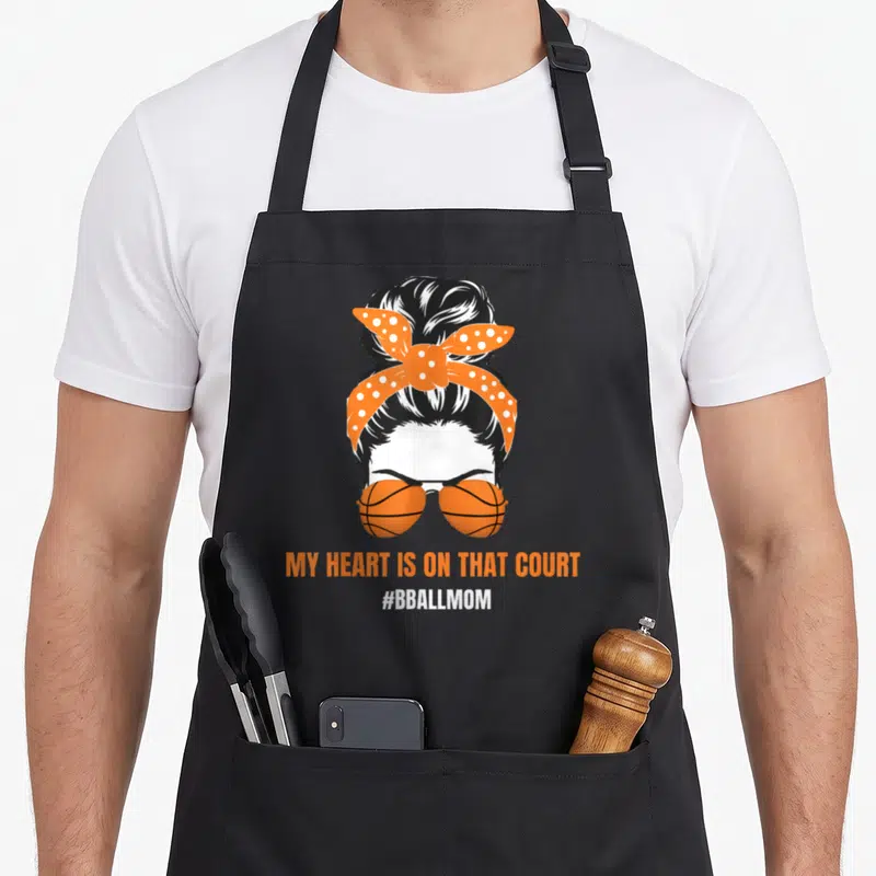 Bball messy aprons - Woman with bun, polka dot bandana, basketball sunglasses, and court quote text — shown on a black cotton canvas apron against a white background