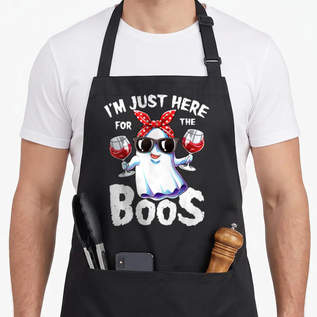 Boo ghost halloween apron - Cartoon ghost in sunglasses holding two red wine glasses under arched text reading I'M JUST — shown on a black cotton canvas apron against a white background