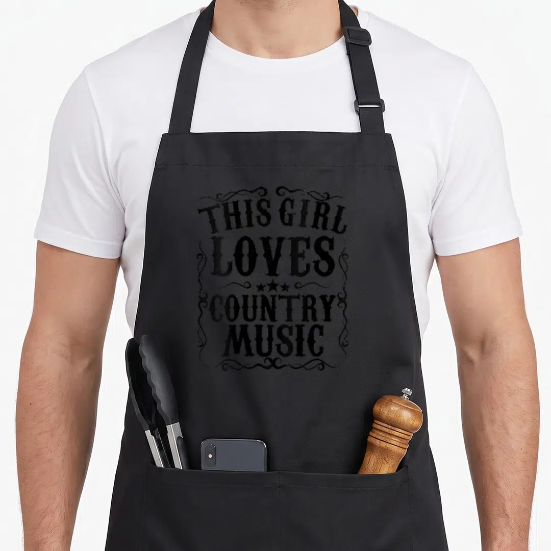 Music concert country kitchen apron - Black distressed text THIS GIRL LOVES COUNTRY MUSIC framed by swirls and three — shown on a black cotton canvas apron against a white background