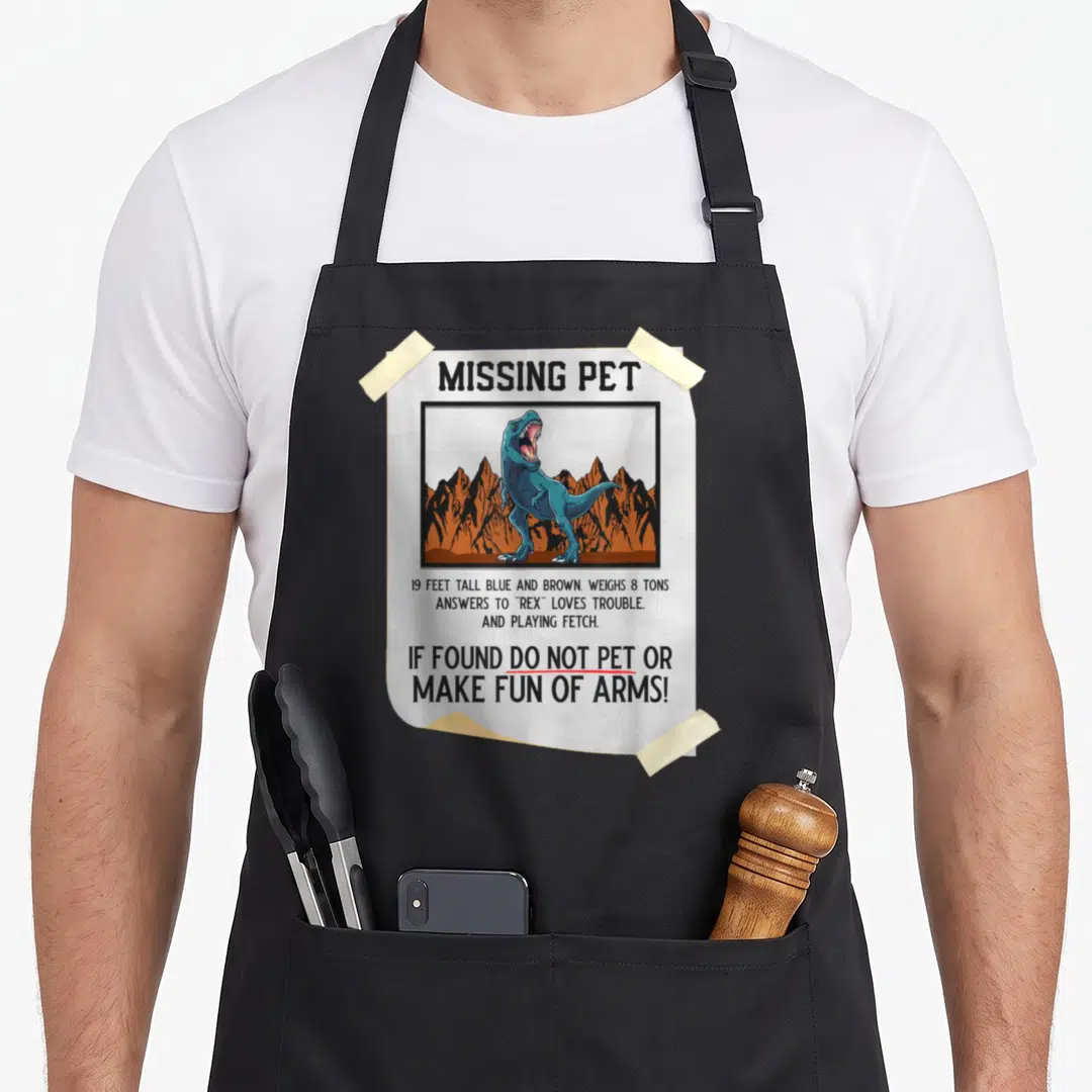 Halloween pet apron - Missing Pet flyer with blue T-Rex illustration and humorous text warnings on black fabric — shown on a black cotton canvas apron against a white background