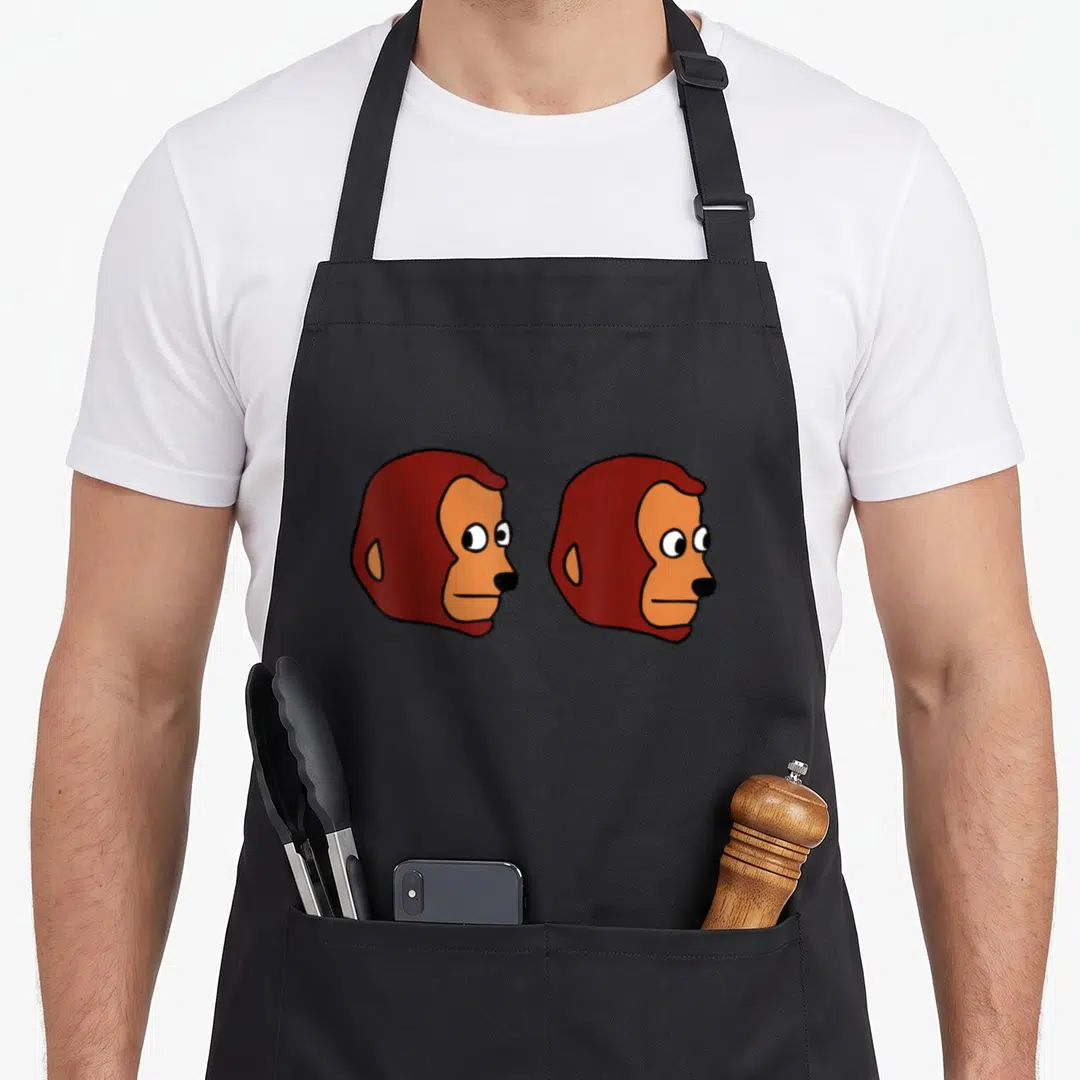 Monkey meme apron - Two identical cartoon monkey heads in profile with brown fur and tan faces side by side — shown on a black cotton canvas apron against a white background