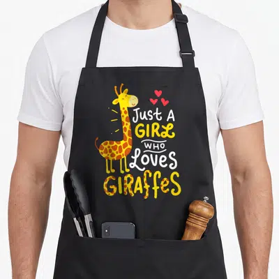 Funny giraffe apron - Cartoon giraffe with brown spots, three red hearts, and stacked text reading Just A GIRL Who — shown on a black cotton canvas apron against a white background