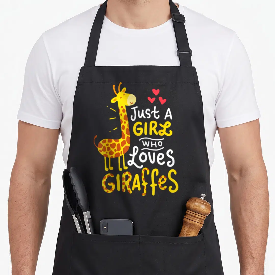 Funny giraffe apron - Cartoon giraffe with brown spots, three red hearts, and stacked text reading Just A GIRL Who — shown on a black cotton canvas apron against a white background