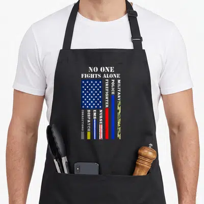 Fight 4th of july apron - No One Fights Alone text above distressed flag and vertical stripes for police, fire — shown on a black cotton canvas apron against a white background